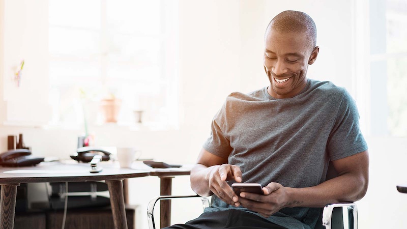 Man using his smartphone while sitting on a chair near a desk. Man using his smartphone while sitting on a chair near a desk.